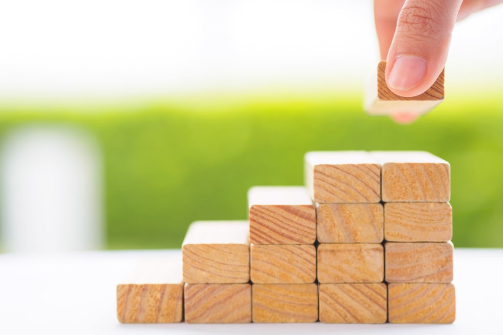 A hand placing a wooden block on a pyramid made of wooden blocks.